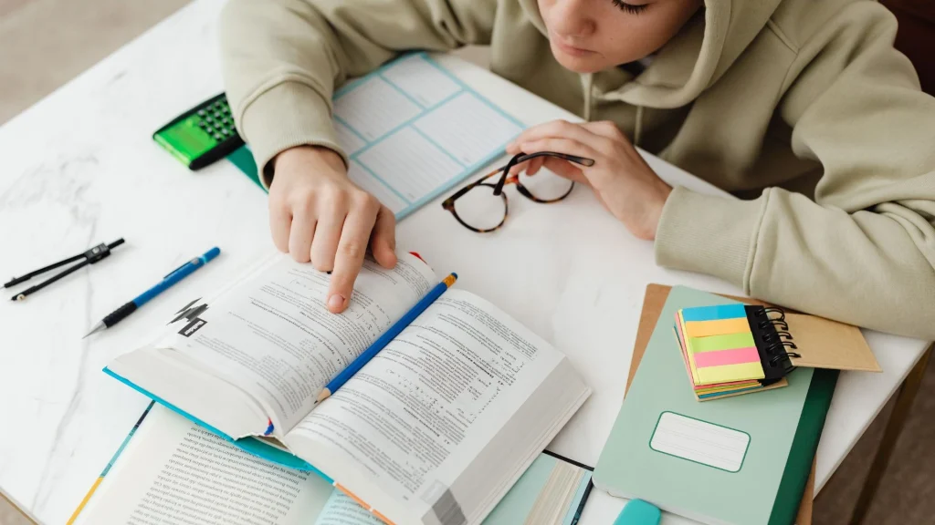 SAT vs ACT test prep - student comparing questions in a study book at a desk with notes and school supplies.